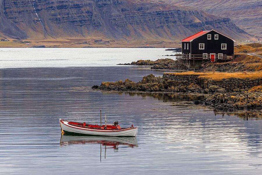 A small boat and a black wooden house along the coast on an autumn day in the Eastfjords, Iceland.